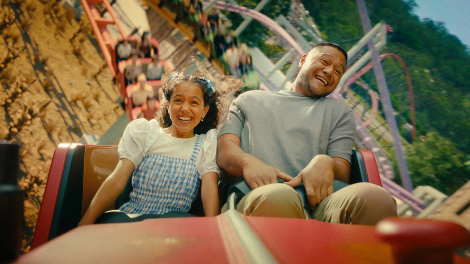 Dad and girl smiling with excitement while riding a high-speed roller coaster at Warner Bros. Movie World Gold Coast.