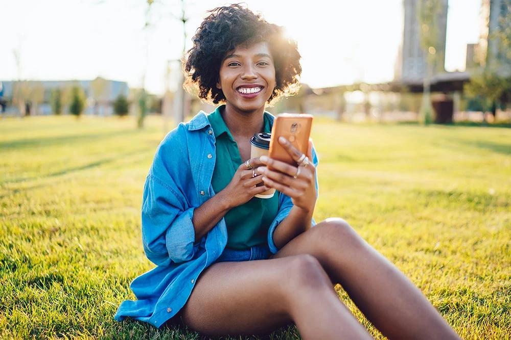 Jeune femme souriante avec un smartphone à la main assise sur l'herbe