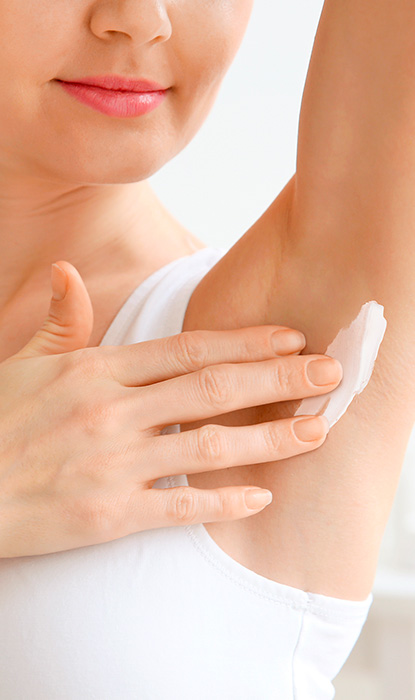 Ung kvinna applicerar kräm på hennes armhåla