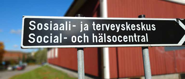 Kuva tiekyltistä, jossa lukee Sosiaali- ja terveyskeskus, sekä sama ruotsiksi alapuolella.