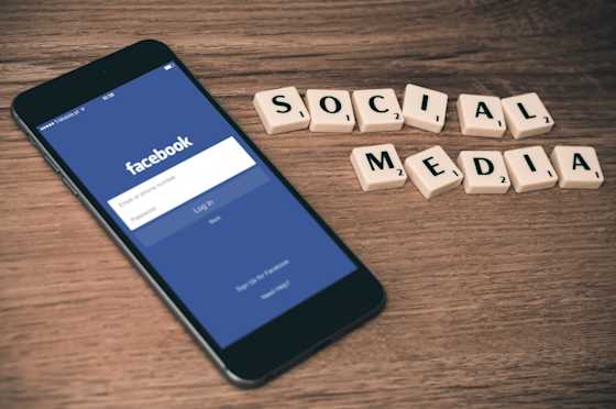 Puhelin, jossa on auki Facebookin sovellus odottamassa kirjautumistietoja sekä Scrabble-pelistä tutuilla nappuloilla tehty teksti "Social media"