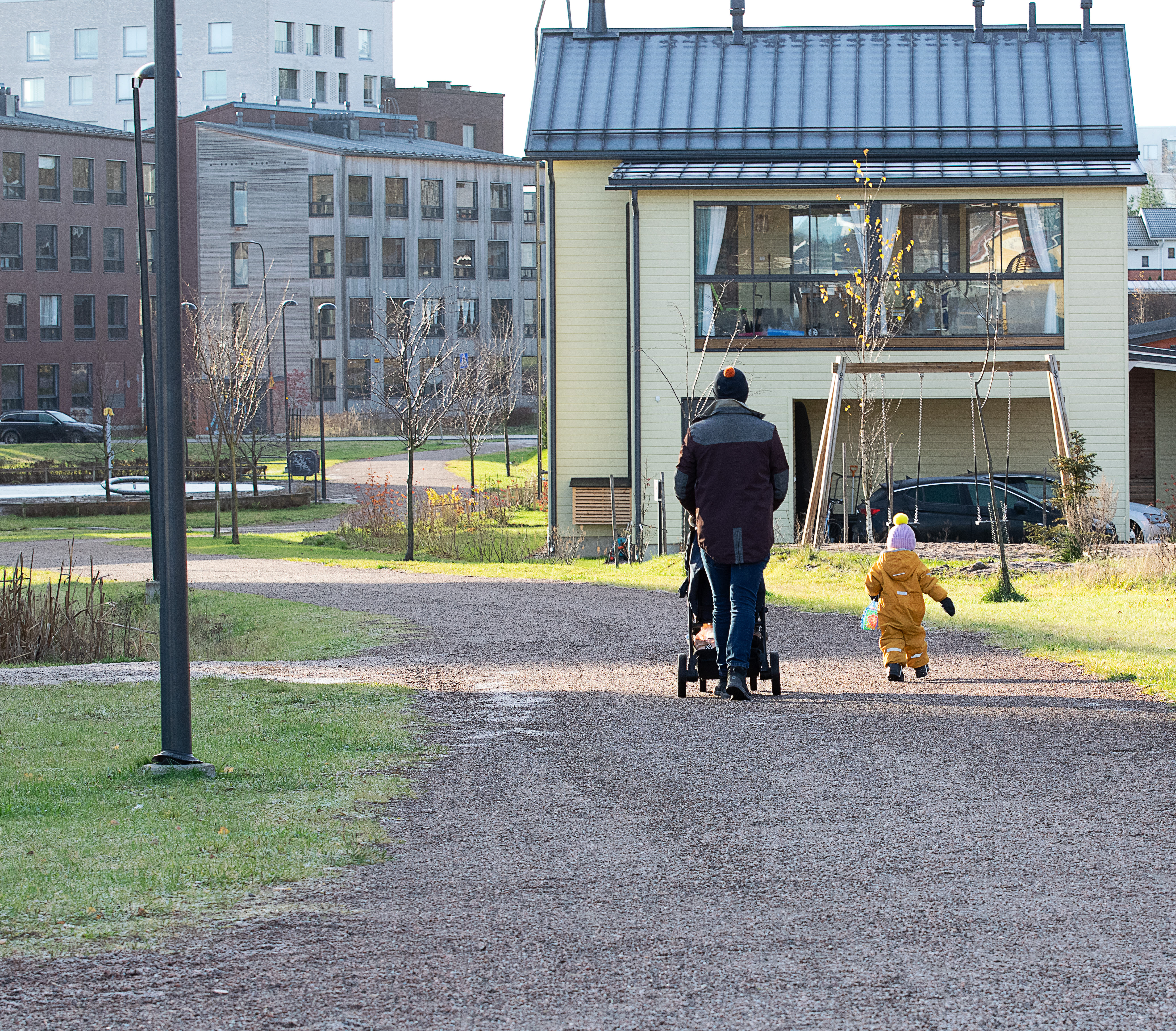 Lauri Lavanti työntämässä rattaita hiekkatietä, vieressä lapsi kävelee ja taustalla on taloja.