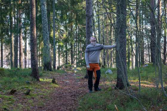 Lauri Lavanti retkeilyvaatteissa metsässä, nojaa puuhun ja katsoo ylös sen runkoa