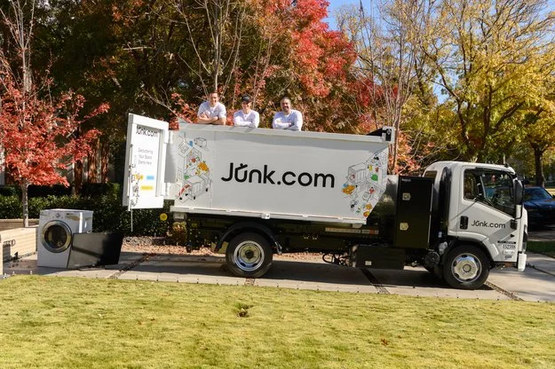 Junk.com junk truck sits in a driveway of a house with a clean lawn.