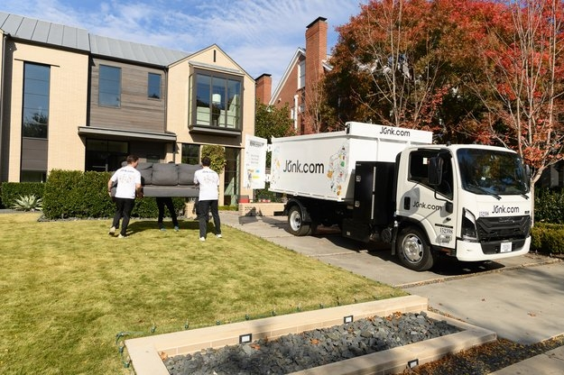 Junk haulers from Junk.com carry a couch out to the junk truck from a modern home.