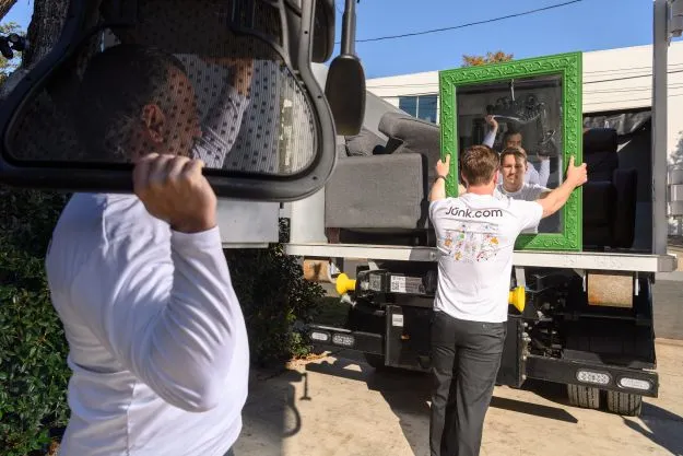 Junk.com team members help clear a cluttered room by removing chairs and mirrors and hauling them into the junk truck. 