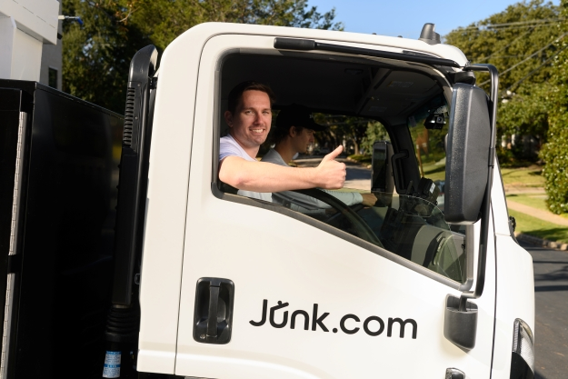 Junk.com team member flashes a smile and a thumbs up from the passenger's seat of a Junk.com truck.