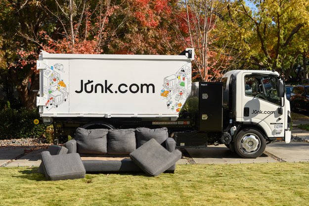 A bulk piece of clutter, an old couch, sits by a Junk.com same-day junk removal truck.