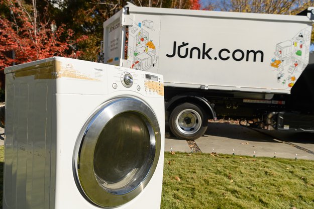 Unwanted washer sits on lawn in front of a same-day junk removal truck from Junk.com.