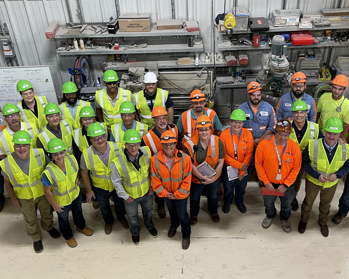 Industrial workers in safety gear pose in warehouse, wearing high-visibility vests and hard hats