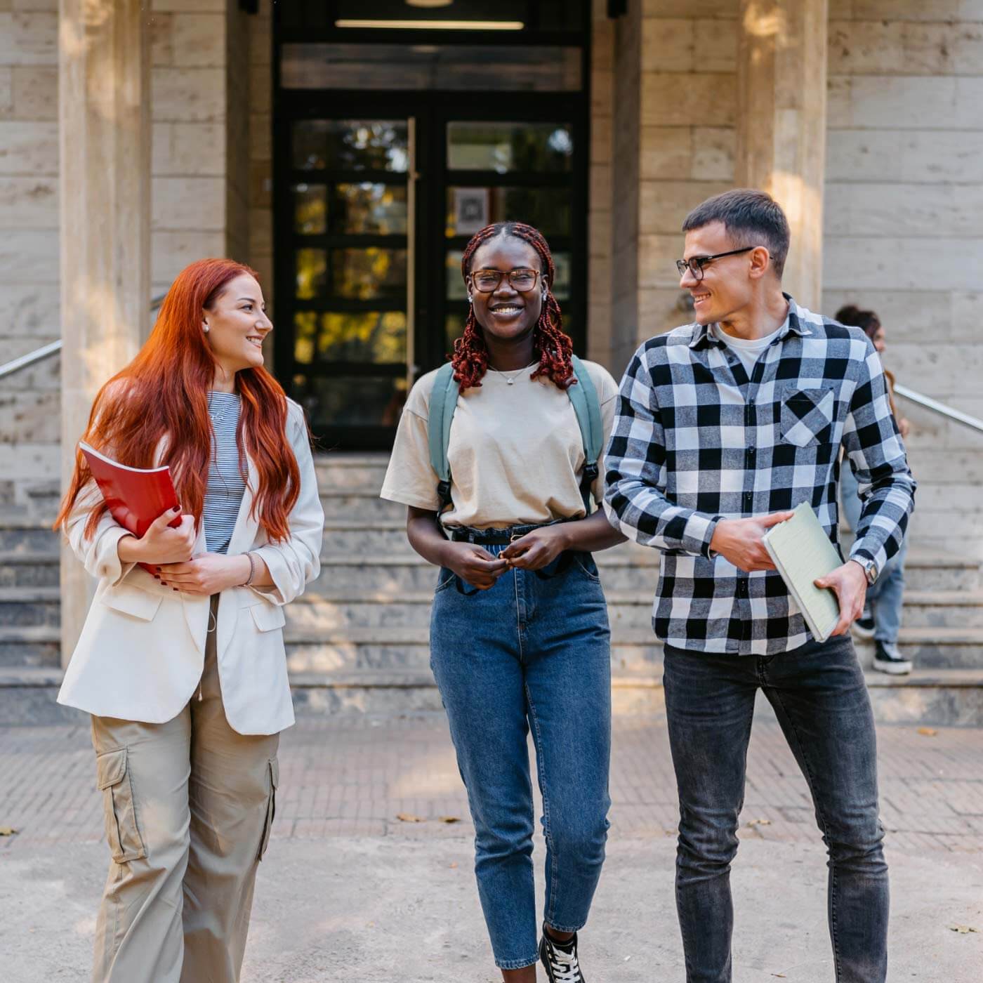 three smiling students holding notes and walking outside a college