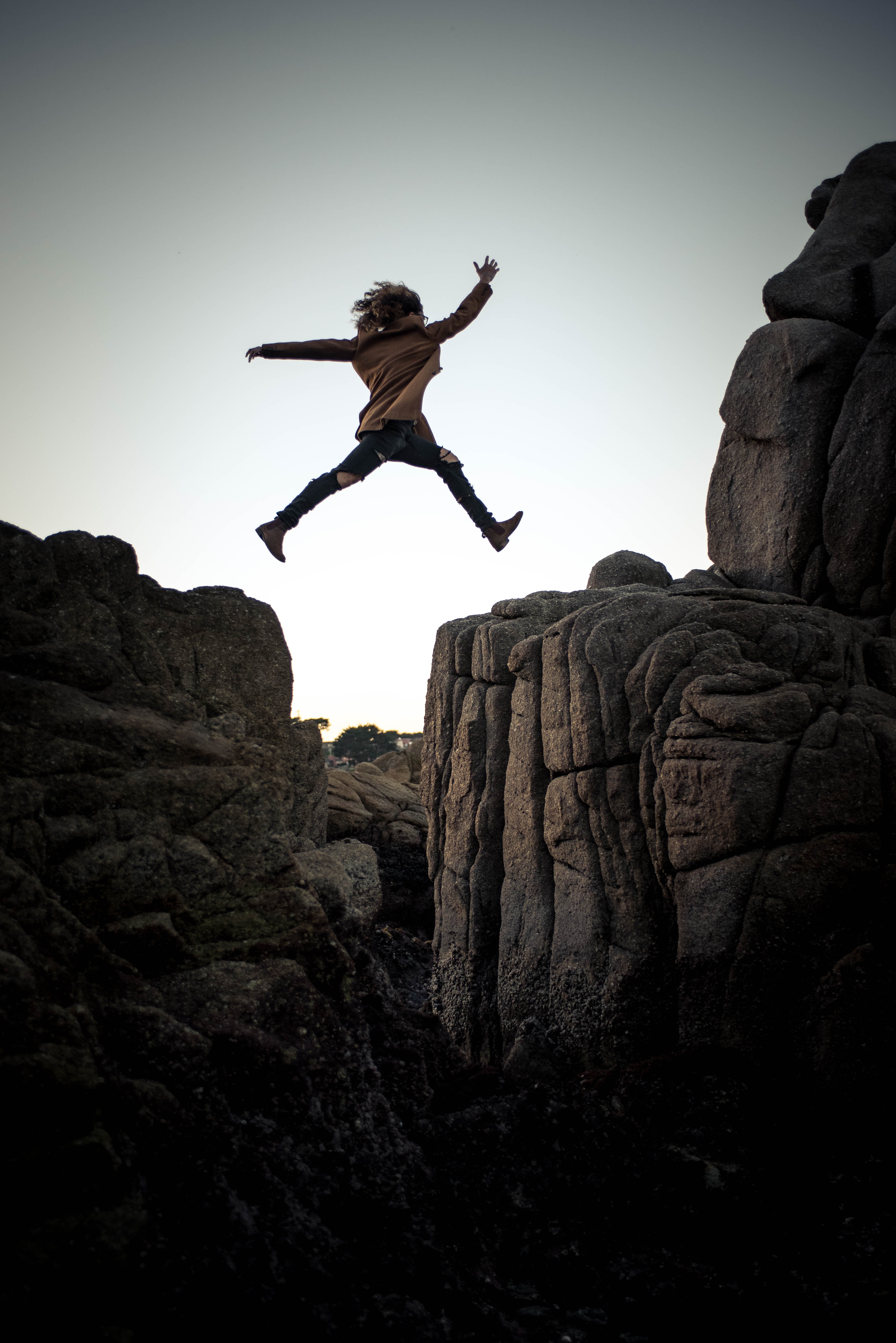 A woman jumps off a cliff into the sunset.