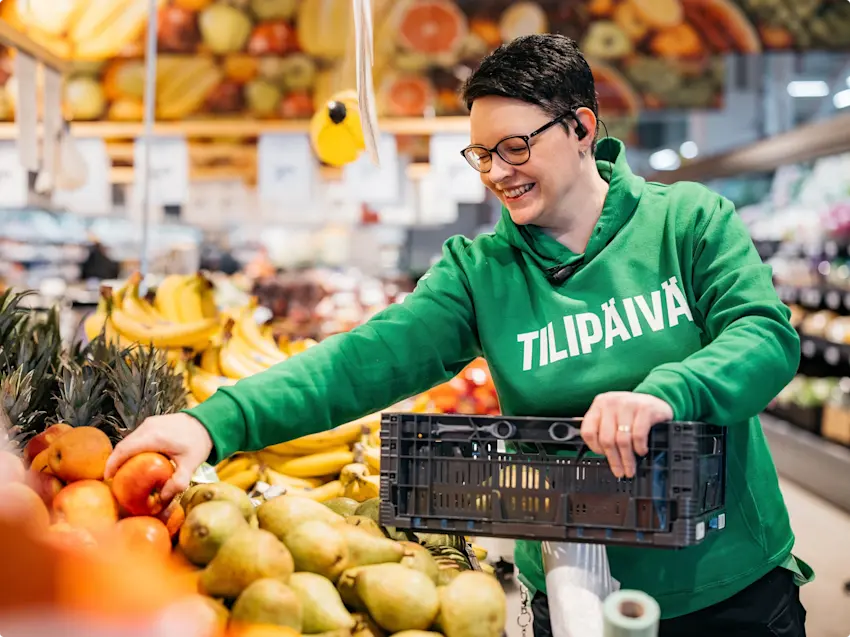 S-Marketin työntekijä tilipäivä hupparissa poimimassa hedelmiä.