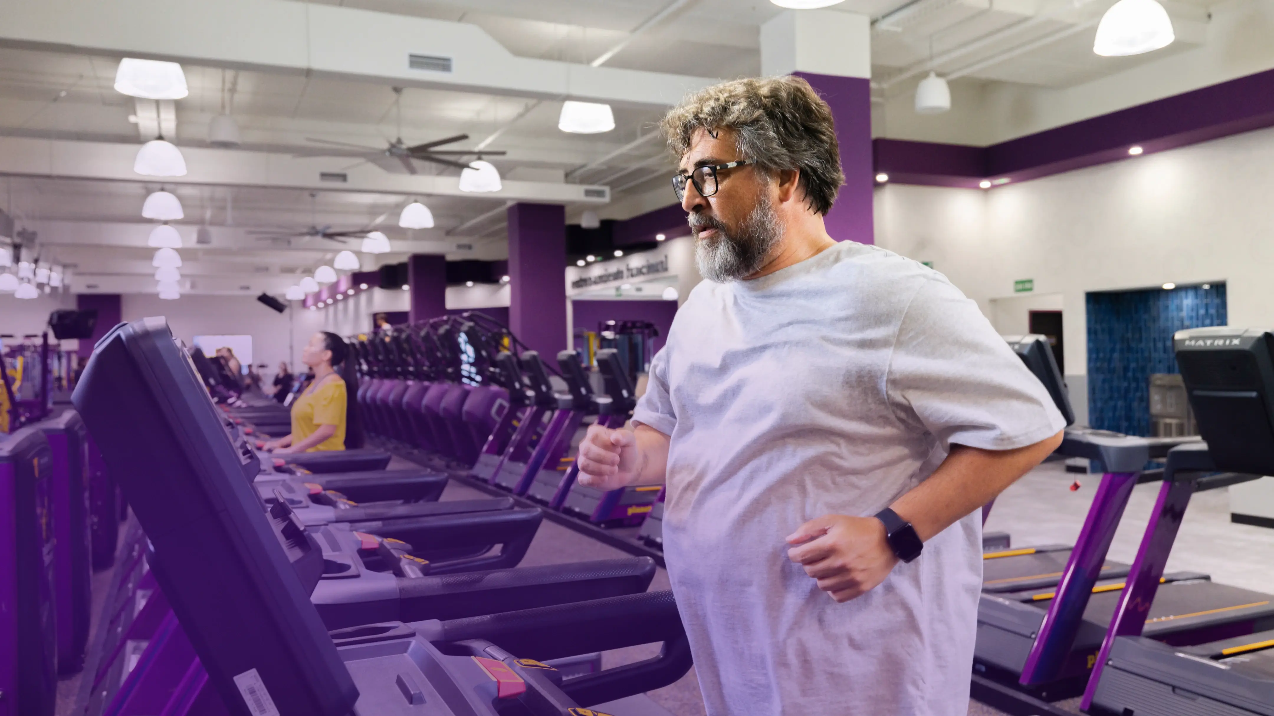 Miembros de Planet Fitness ejercitándose en equipos de fuerza con un amable miembro del personal paseando