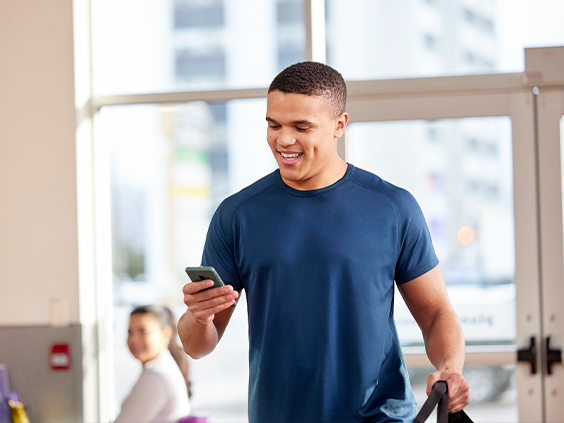 Man in workout clothes looking at phone and smiling in a Planet Fitness club