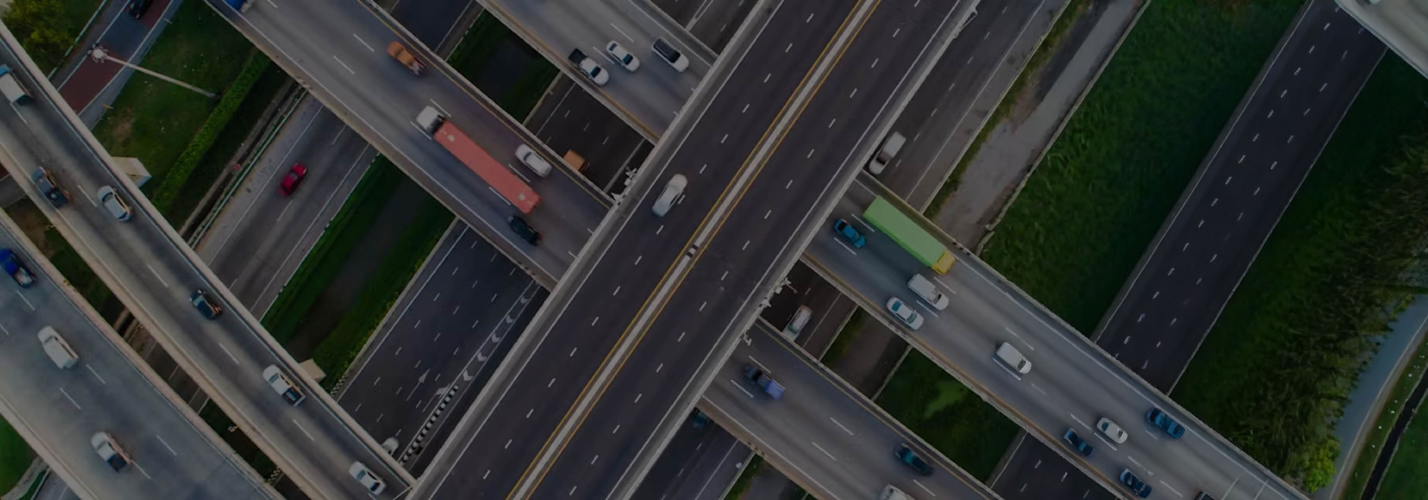 Aerial view of a complex, multi-level highway interchange with cars and trucks traveling on intersecting overpasses and roads.