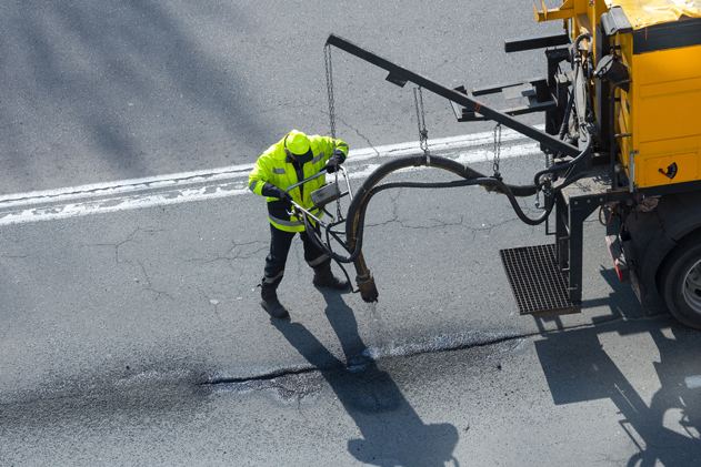 A construction worker in a high-visibility jacket uses equipment to repair a road.
