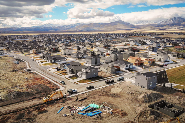 An aerial view shows a new housing development with construction happening in the foreground, and mountains in the background.