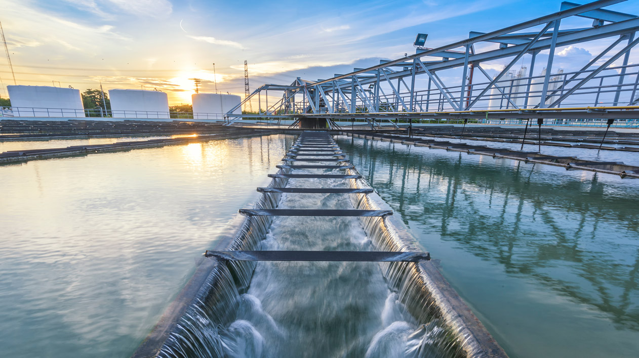 A water treatment facility with flowing water and large industrial structures under a bright sky.