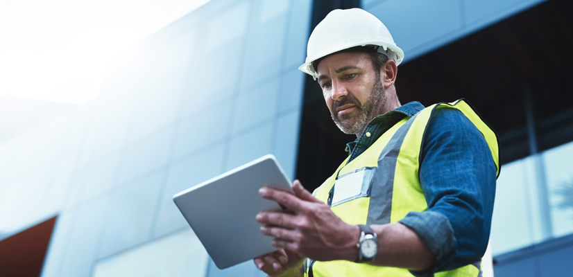 Man in reflective vest and hard hat using tablet in front of building