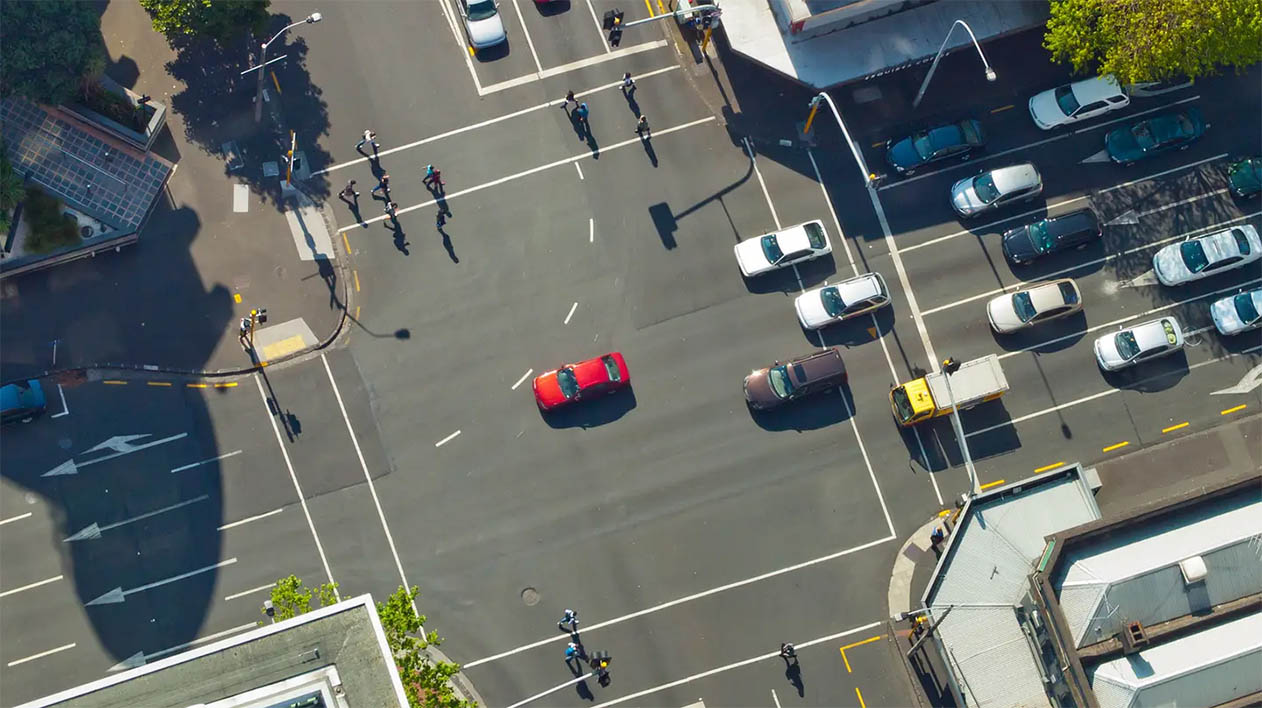An aerial view of a busy city intersection with cars and pedestrians moving in different directions.