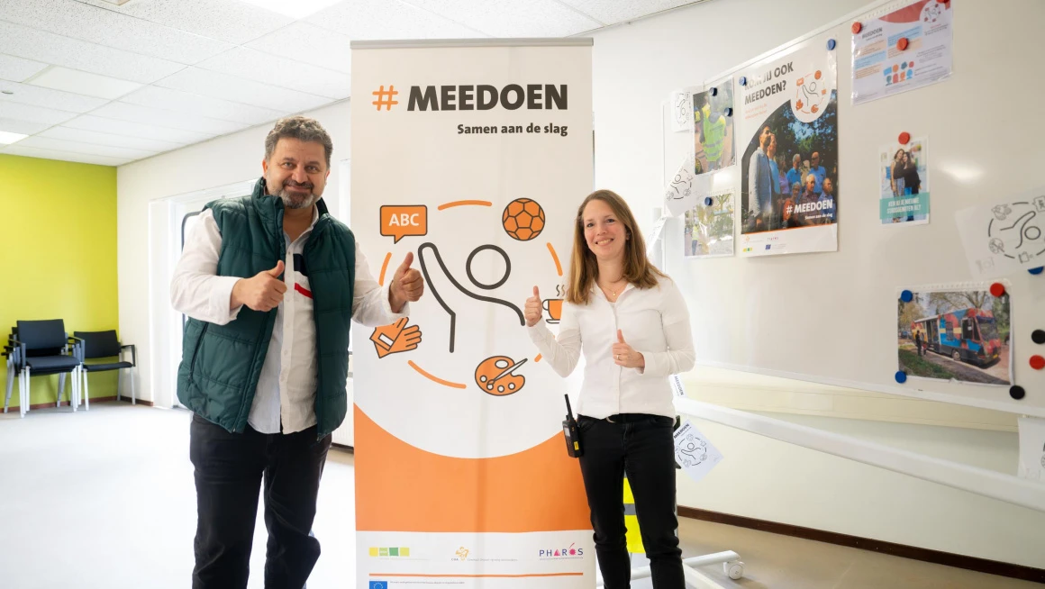 Two people stand at a sign from the Meedoen desk.