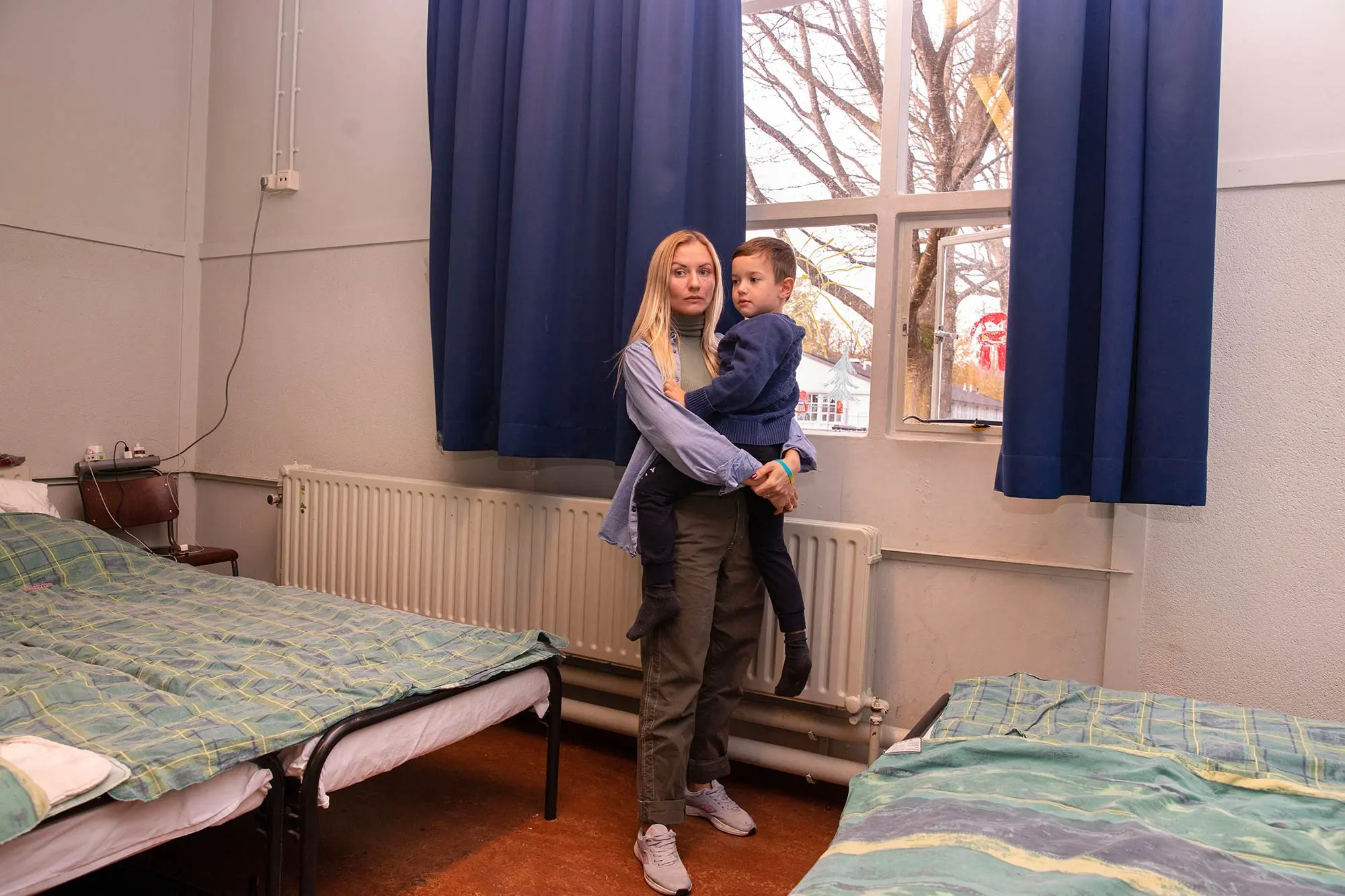 Een vrouw staat in een kamer van de opvang voor Oekraïners. Ze draagt haar kind in haar armen. 
