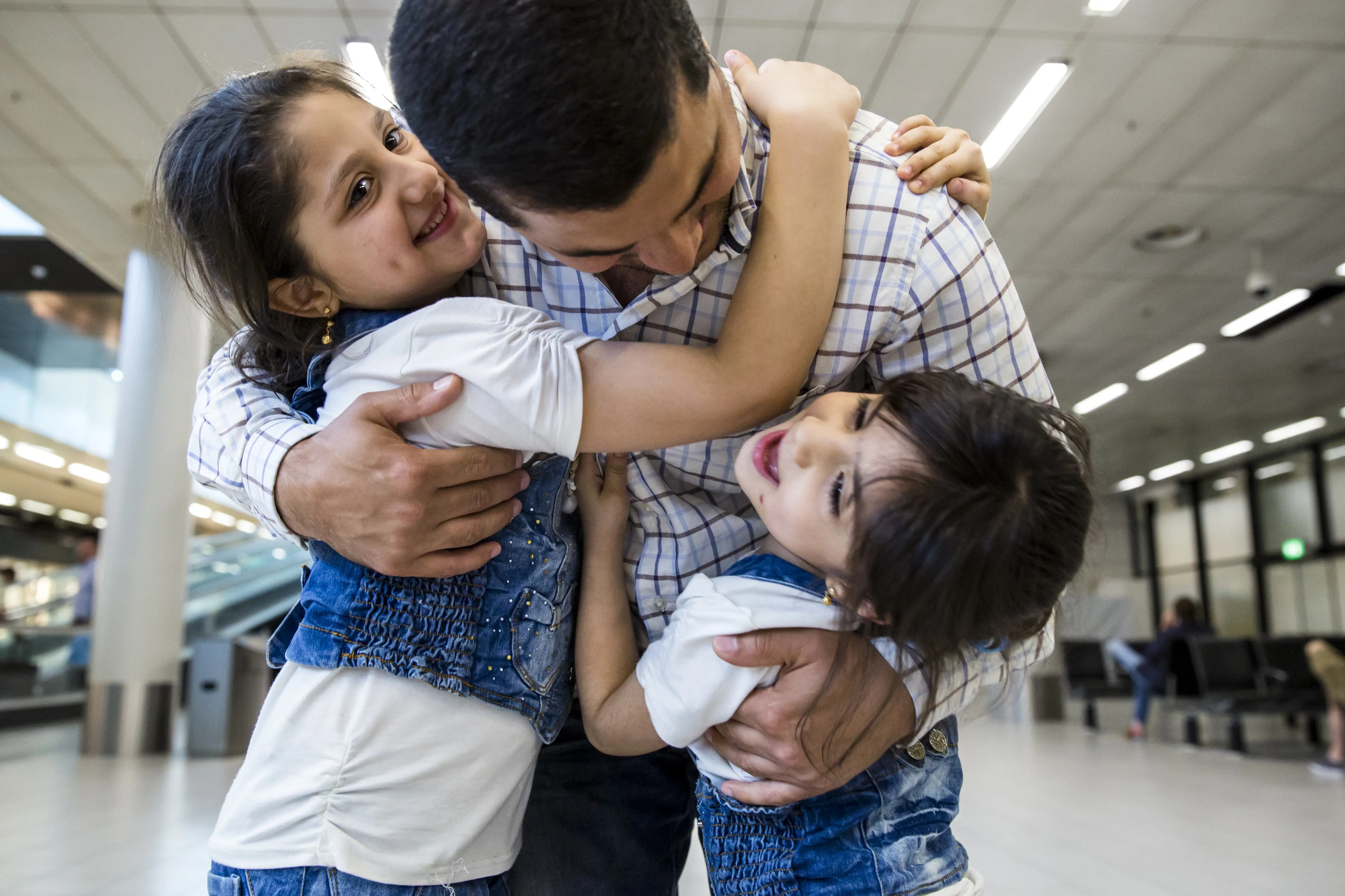 A father can finally hold his two daughters again after family reunification at Schiphol Airport.
