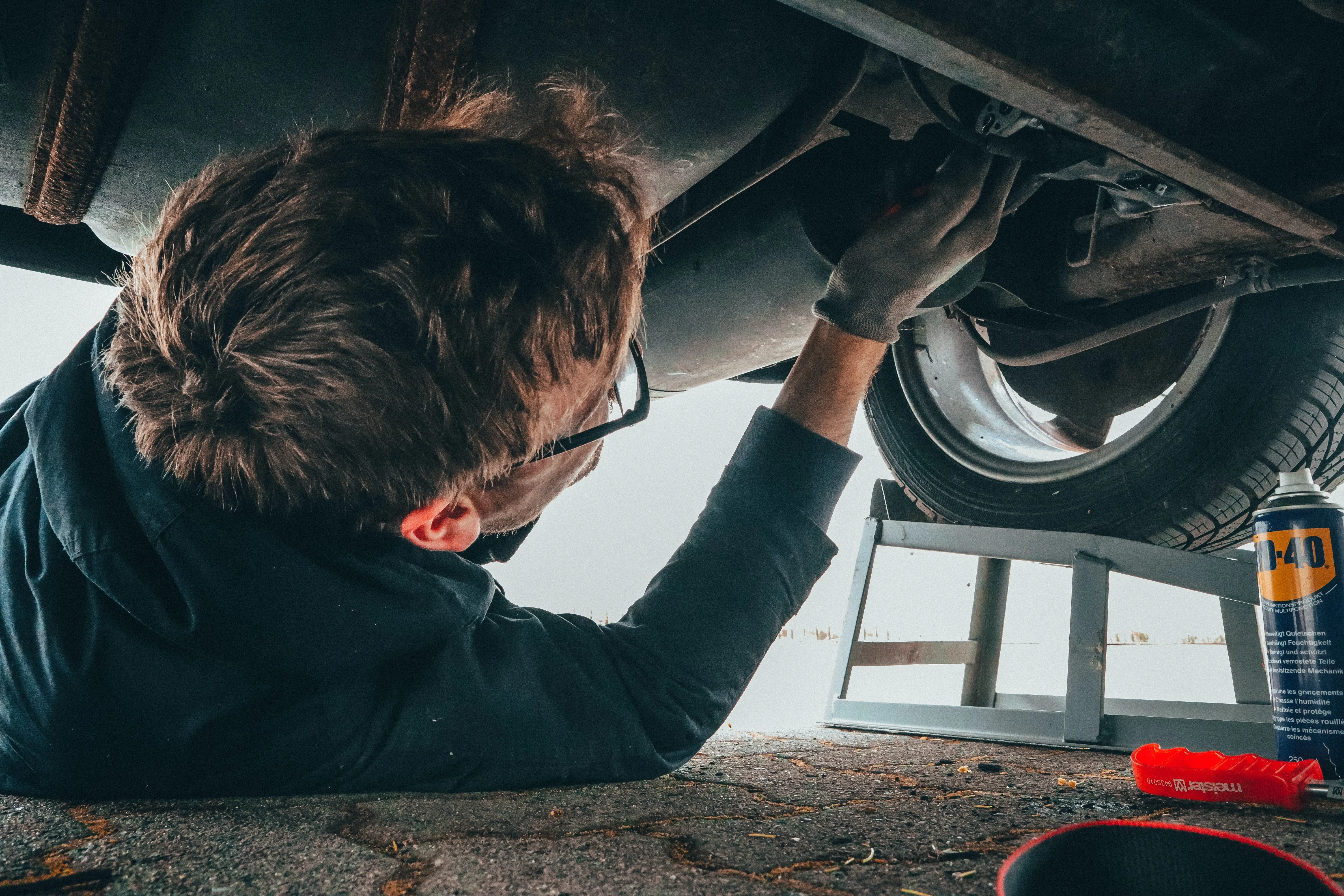 A man lies on the ground repairing the underside of his car.