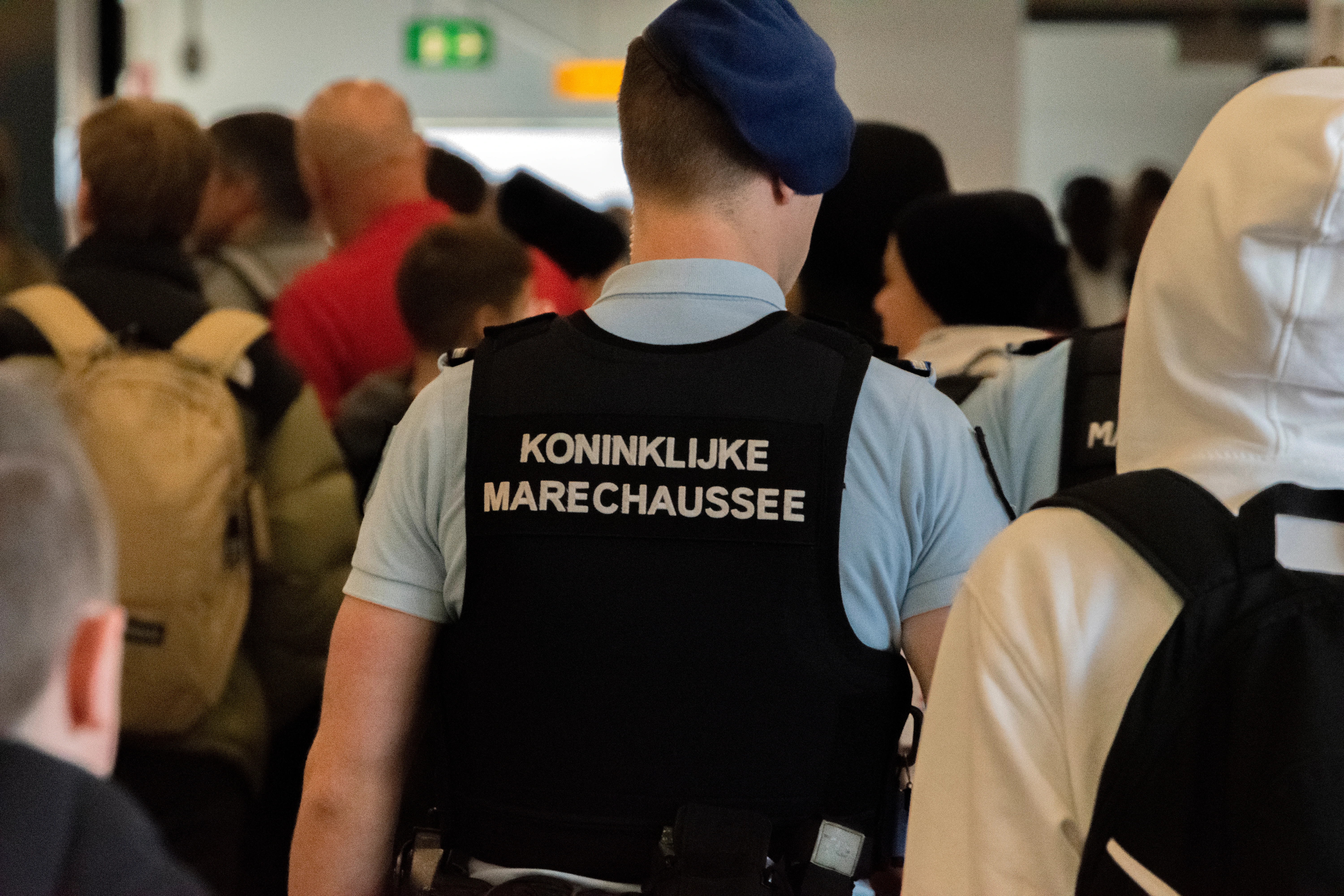 Een agent van de Koninklijke Marechaussee loopt op Schiphol tussen de mensen. 