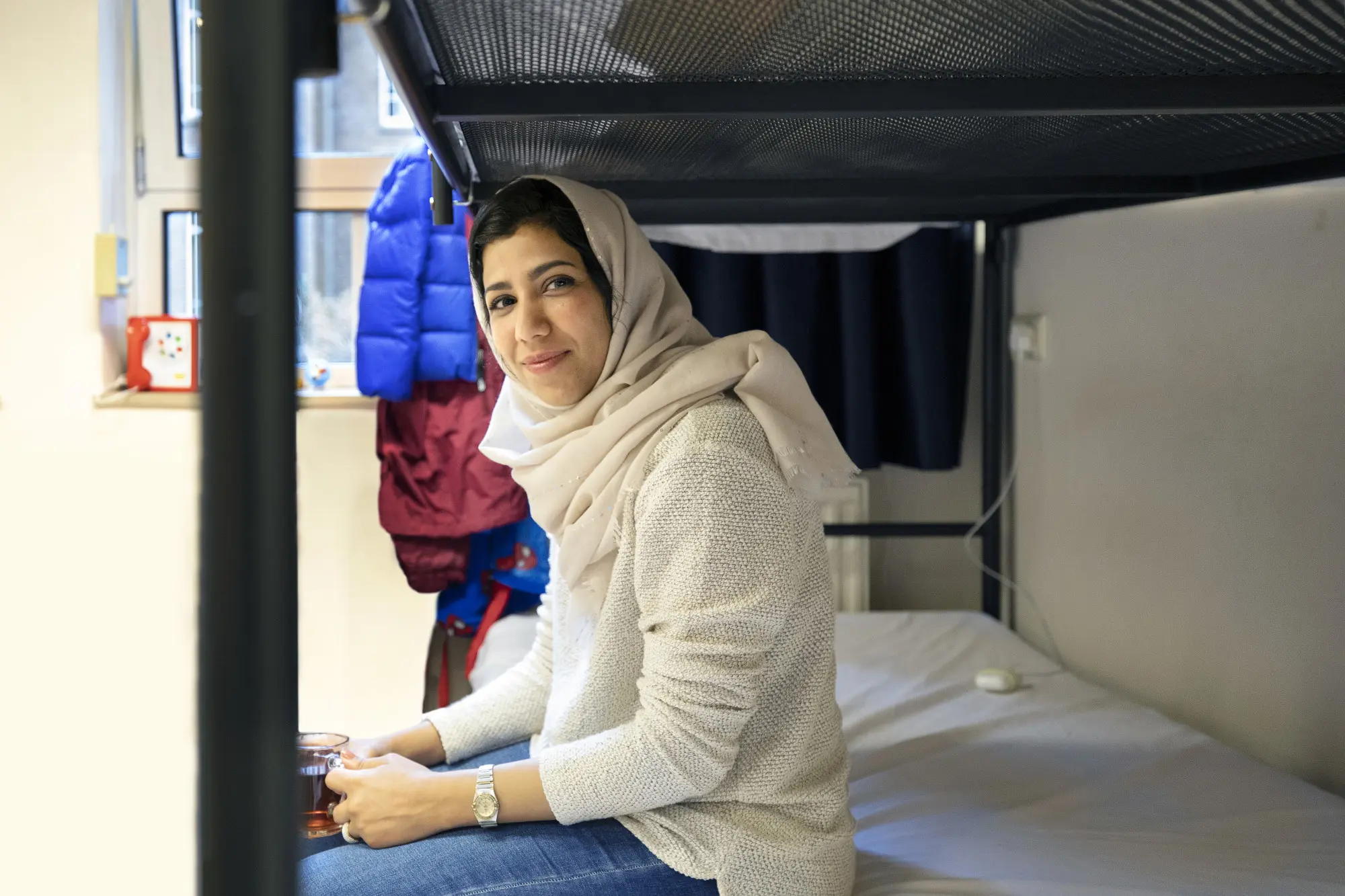 Een jonge vrouw zit op haar in bed in de asielopvang