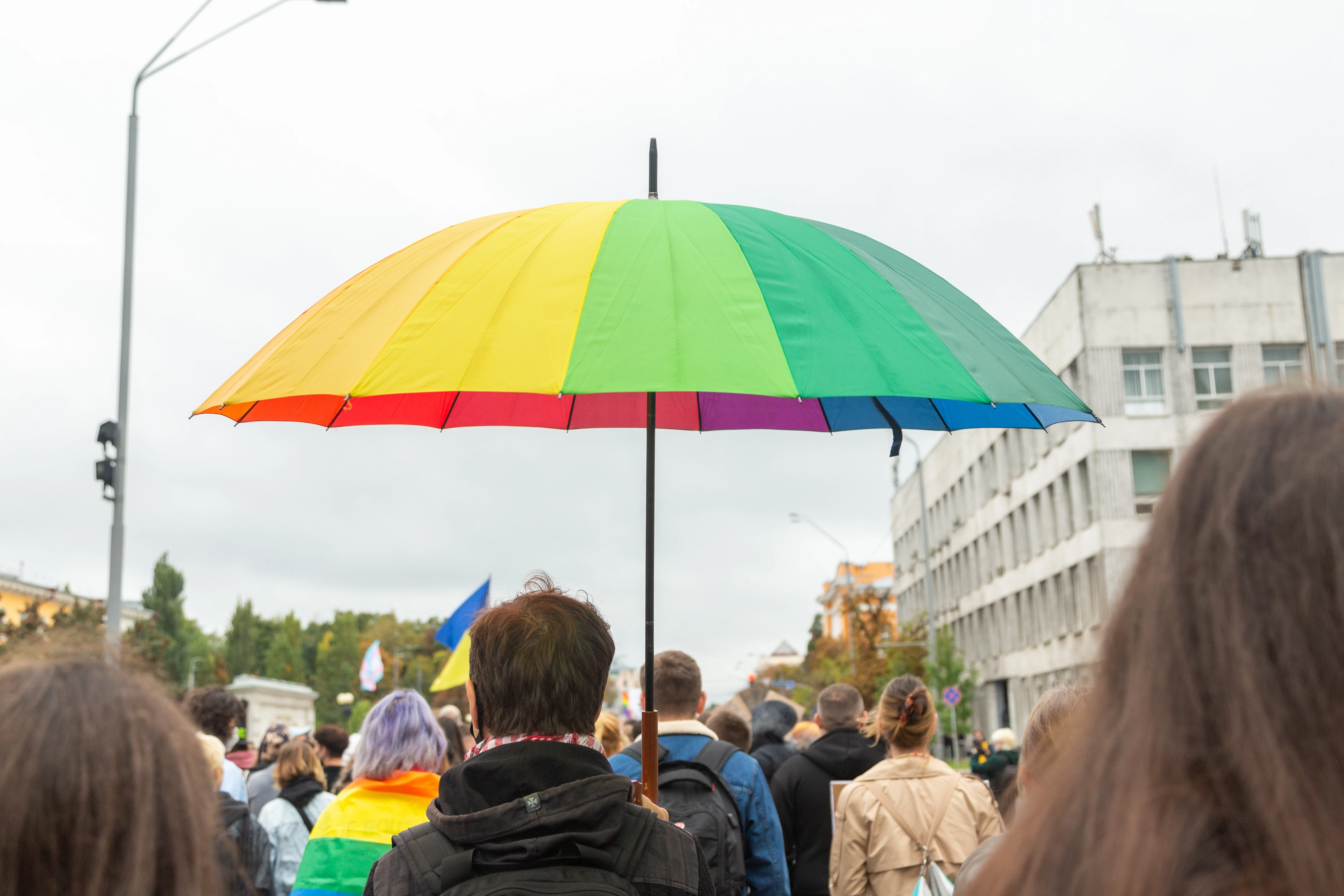 On an overcast grey day, one of the participants in a pride parade in Kiev holds an umbrella in rainbow colours over his head.