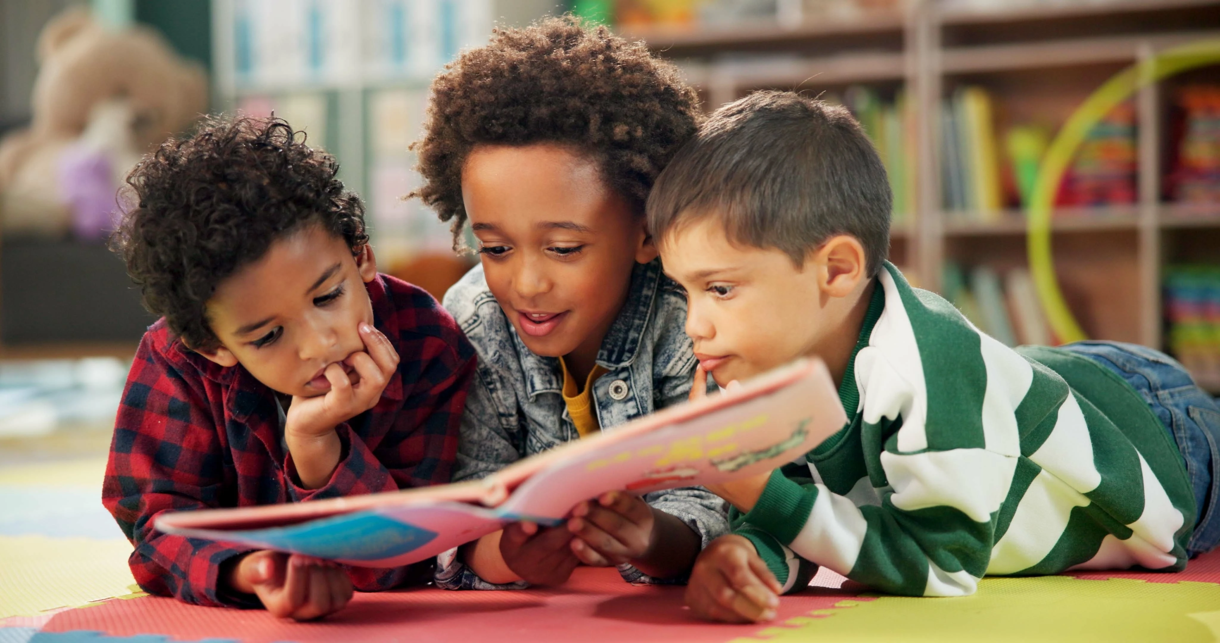 Drie op de grond liggende jongens lezen samen één boek