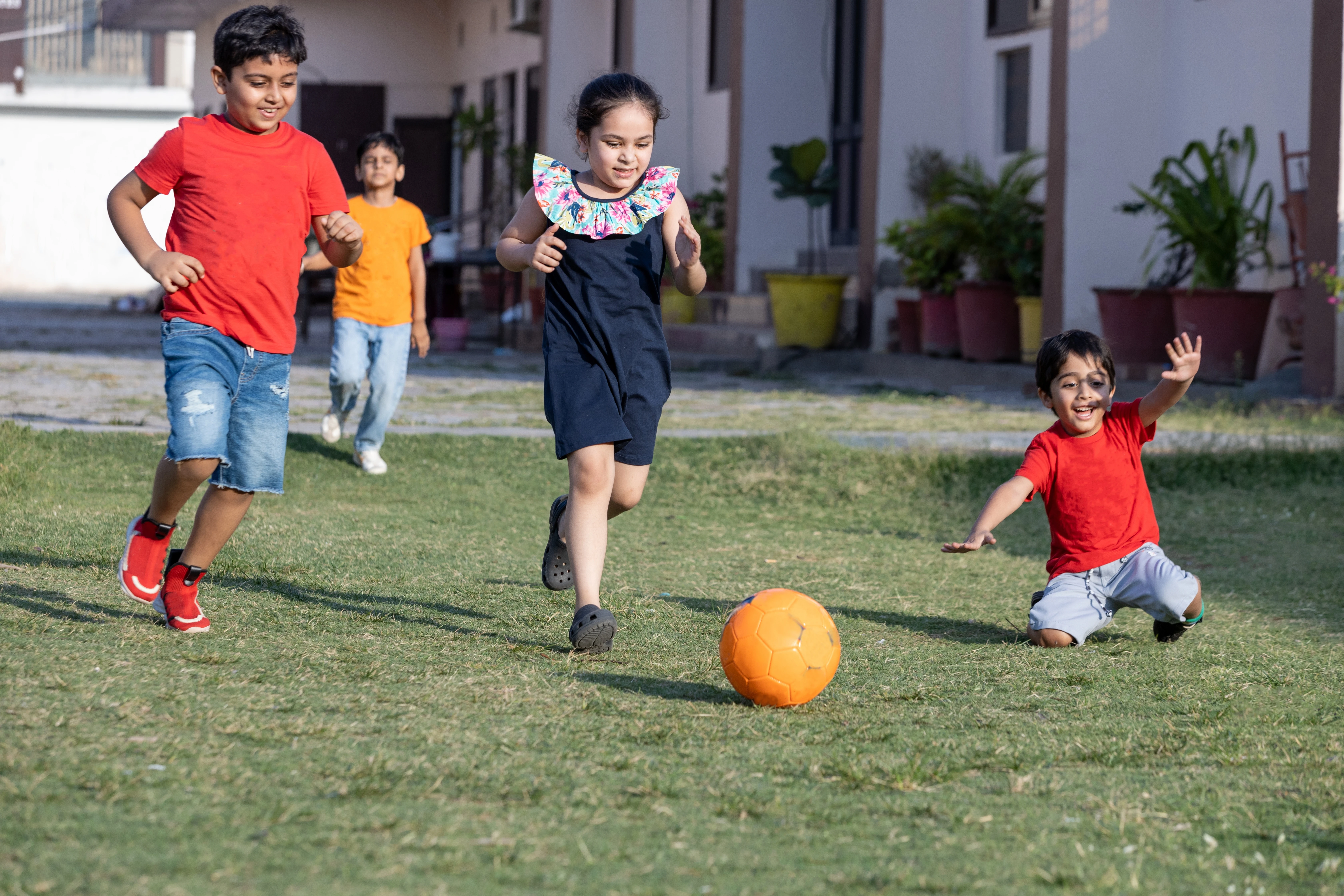 Children in coloured T-shirts run on a lawn chasing an orange ball