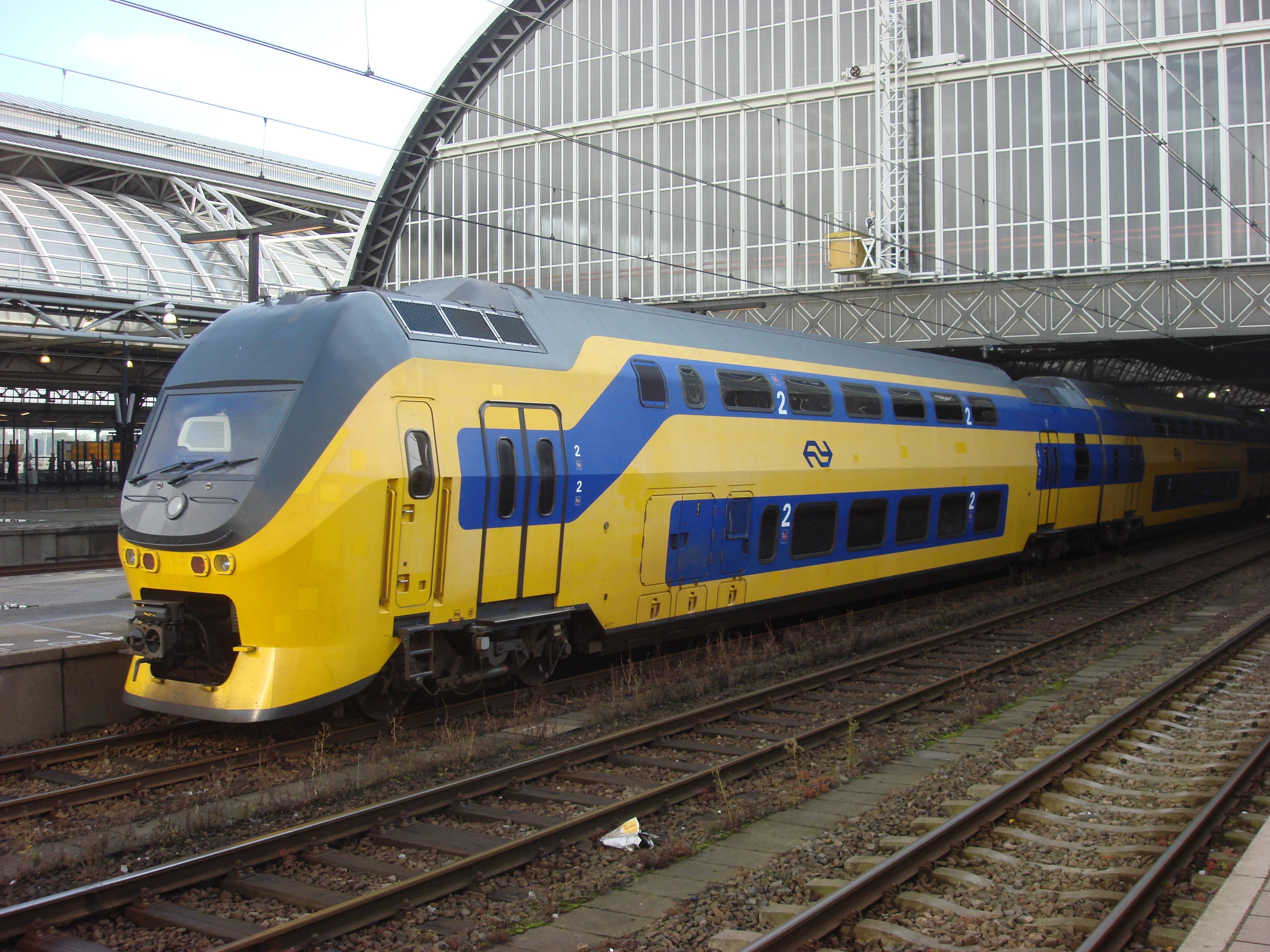 Een geel-blauwe typisch Nederlandse trein die een treinstation uitrijdt. 