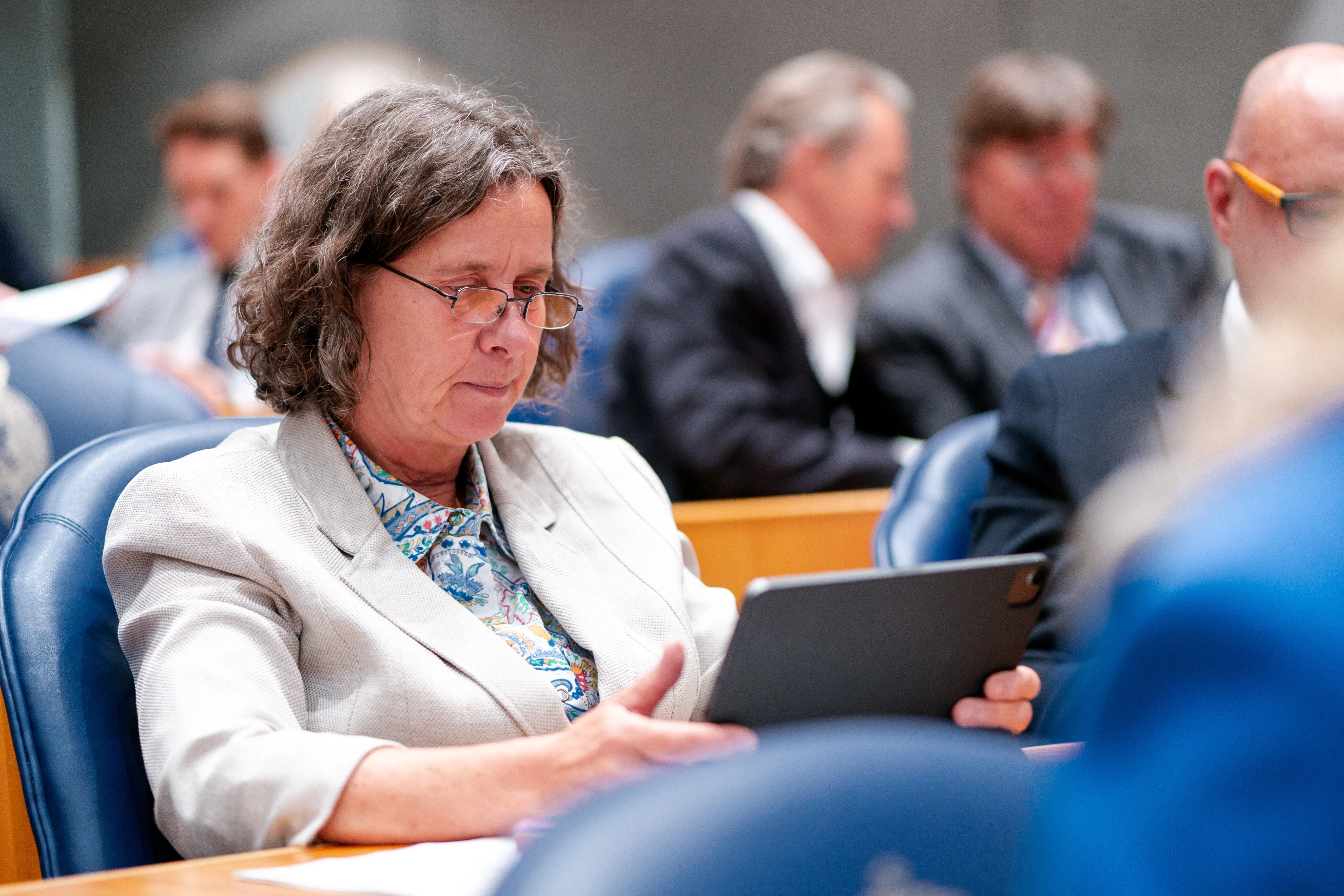 Minister Marjolein Faber zit in de Tweede Kamer en kijkt op haar tablet. 