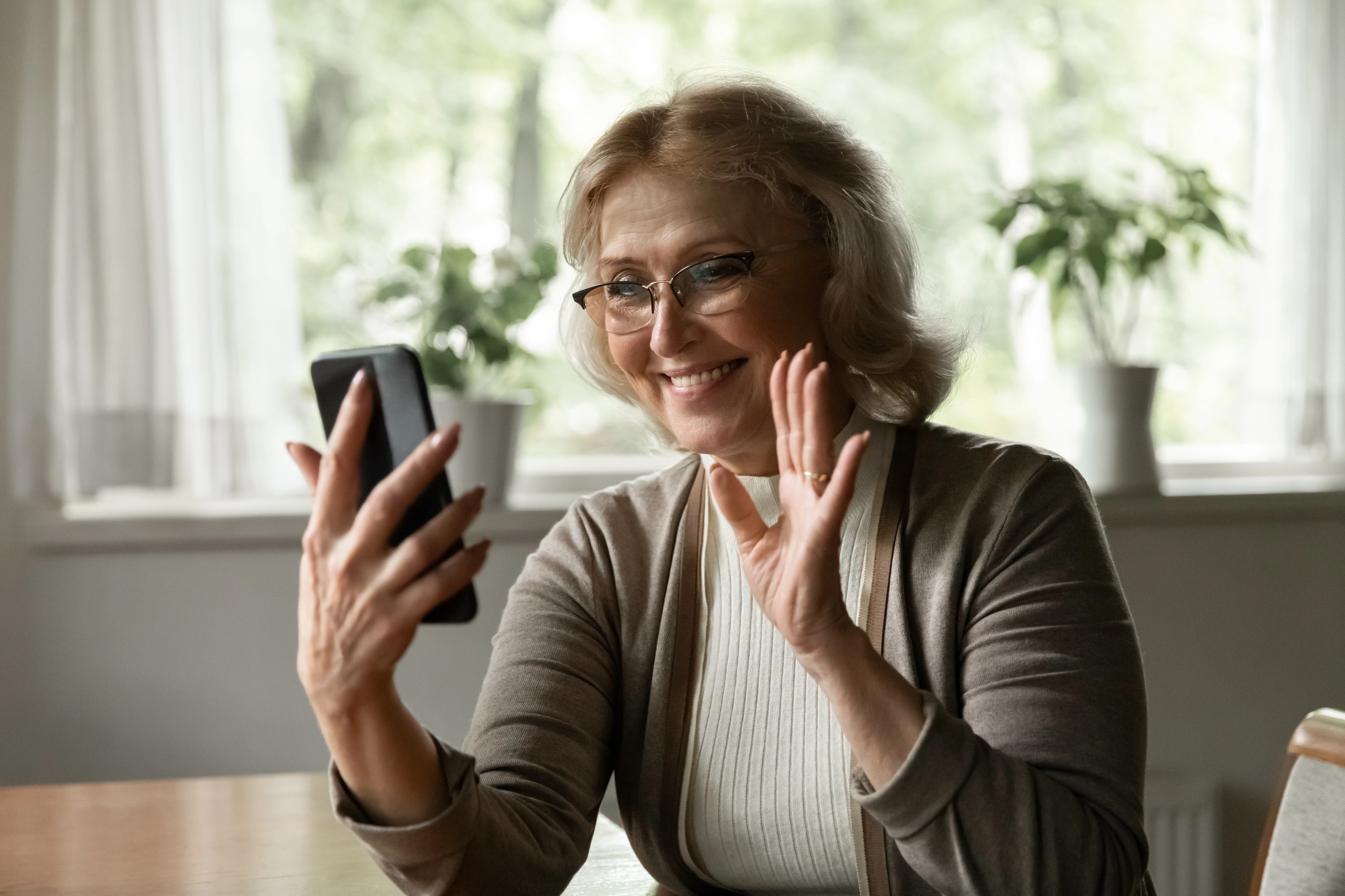 Een vrouw videobelt met haar telefoon en zwaait. 