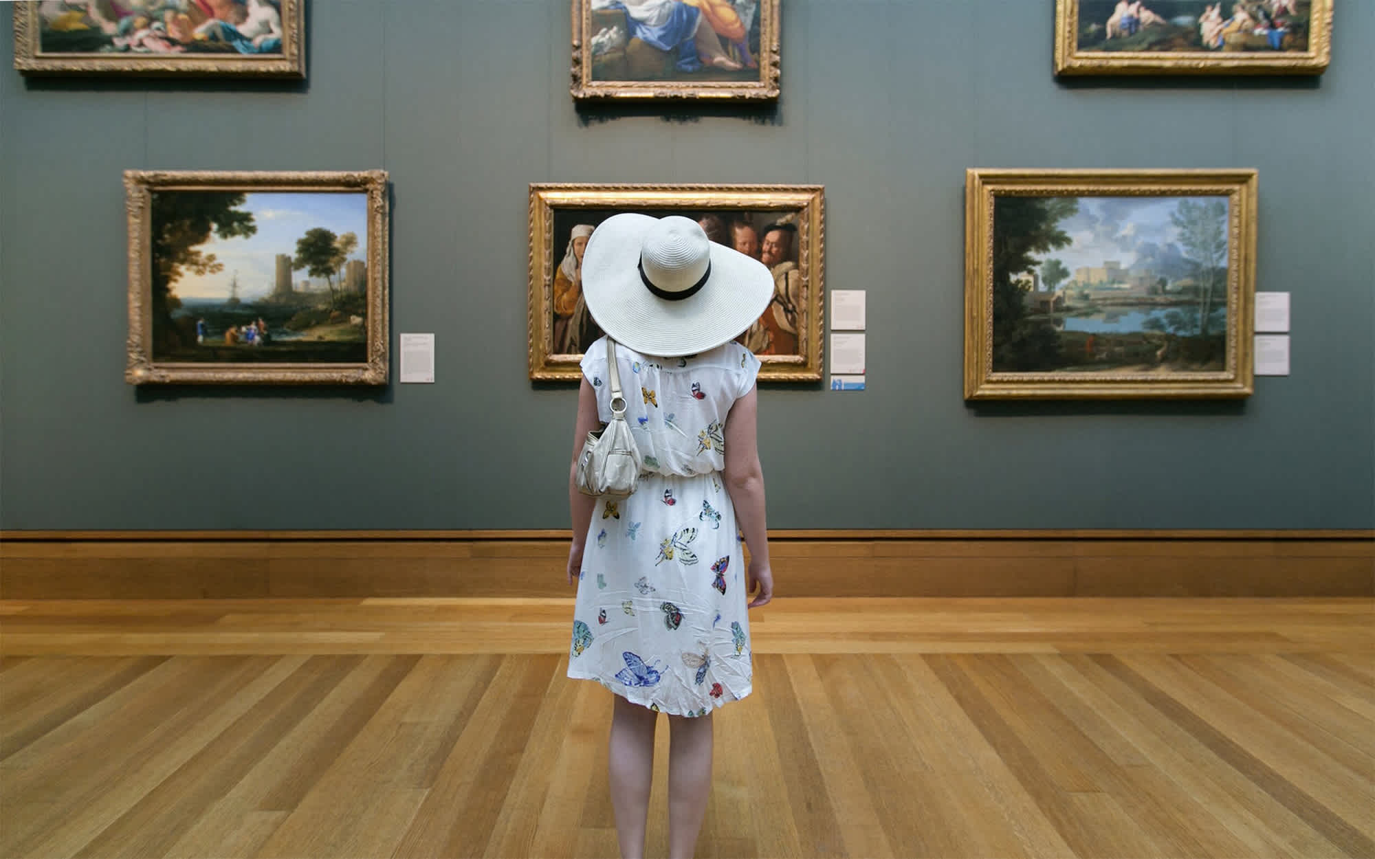 A photo of a woman. She is observing a wall of paintings.