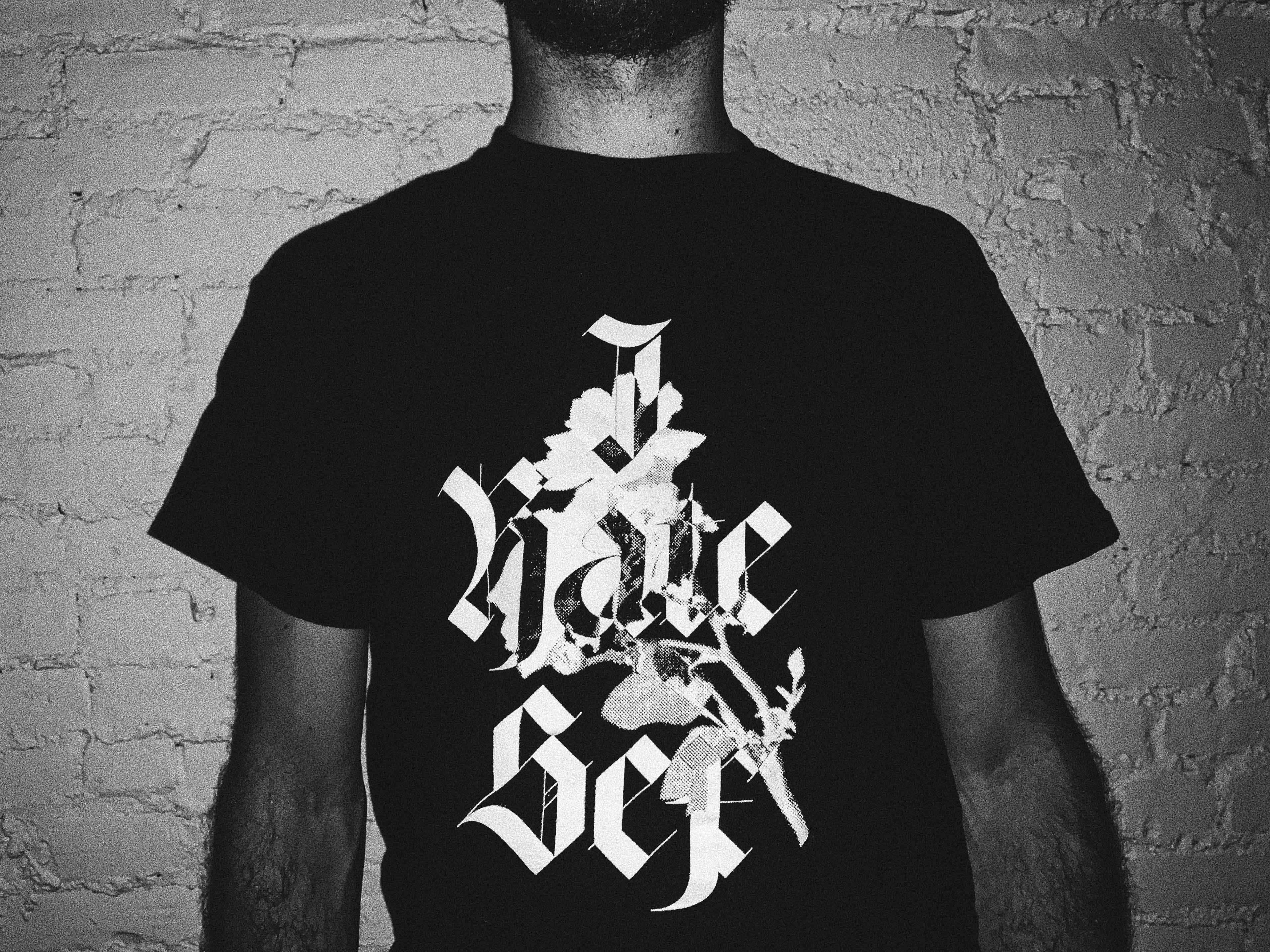 a black t-shirt lays wrinkled on a medium gray background. The text on the shirt reads "I Hate Sex" in a geometric black letter typeface. Overset on the text is an image of a duo-tone rose. The places where the text and rose overlap invert.