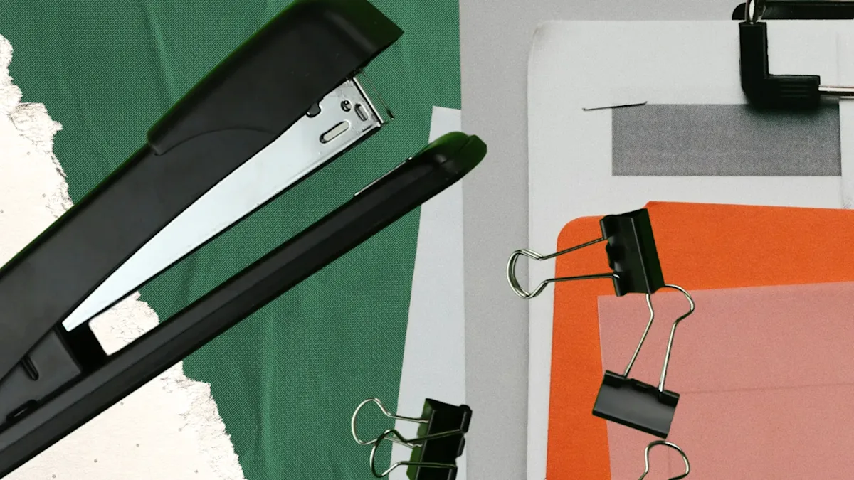 Black stapler and binder clips on green fabric; orange and pink paper with black binder clip on gray surface.