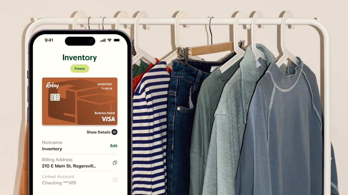 A clothing rack with sweaters and jeans in the back. In the forefront, there is an iPhone screen open to a virtiual credit card titled "Inventory".