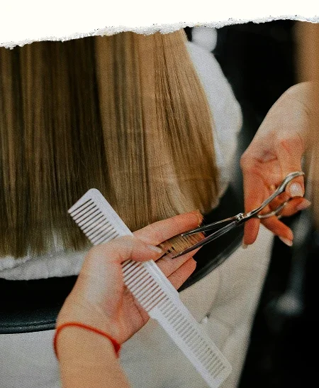 A hairstylist trimming a client’s hair with scissors and a comb, with a torn paper top edge