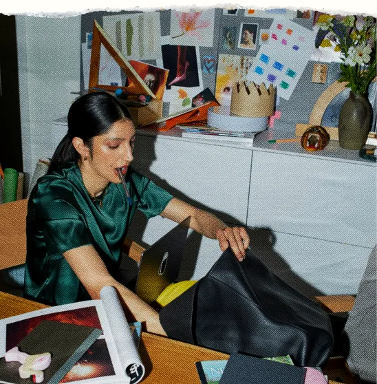 An owner at her desk reaching across a laptop, papers spread in front of her