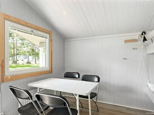 A small room with white paneled walls, a rectangular table, four black folding chairs, a window, and a wall-mounted lamp.