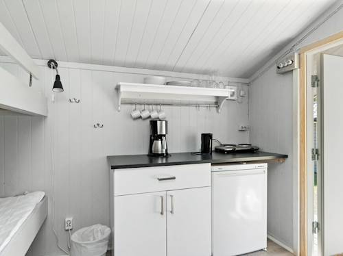 Small kitchenette with white cabinets, a black countertop, coffee maker, electric hot plate, open shelves with dishes, and a mini fridge; bunk bed partially visible on the left.