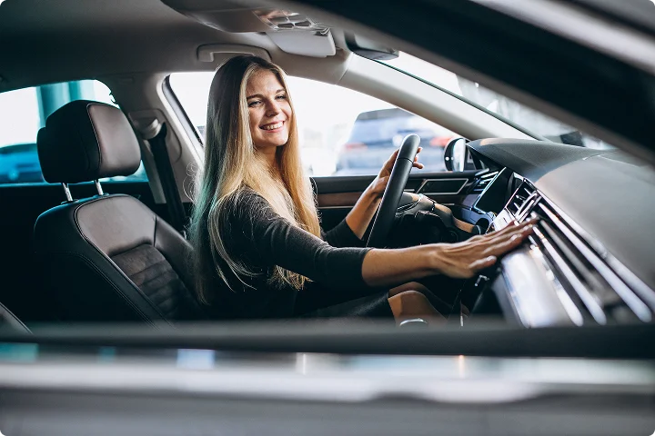 Jauna moteris sėdi vairuotojo vietoje automobilyje, šypsosi ir jungia multimedijos sistemą. Vaizdas perteikia saugumo, pasitikėjimo ir geros nuotaikos jausmą vairuojant.