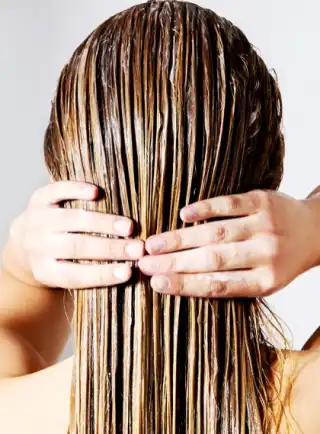 Mujer aplicando producto capilar para cabello maltratado sobre su pelo húmedo