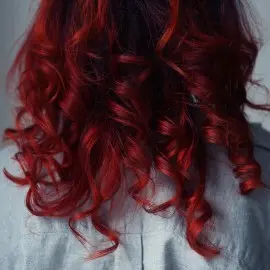 Mujer de espaldas con cabello rizado teñido de rojo, brillante y saludable