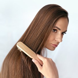 Mujer peinando con un cepillo de madera su cabello liso y sin frizz