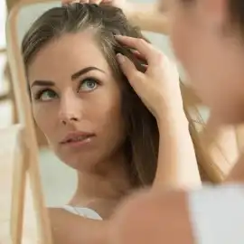 Mujer rubia revisando las raíces de su cabello en un espejo